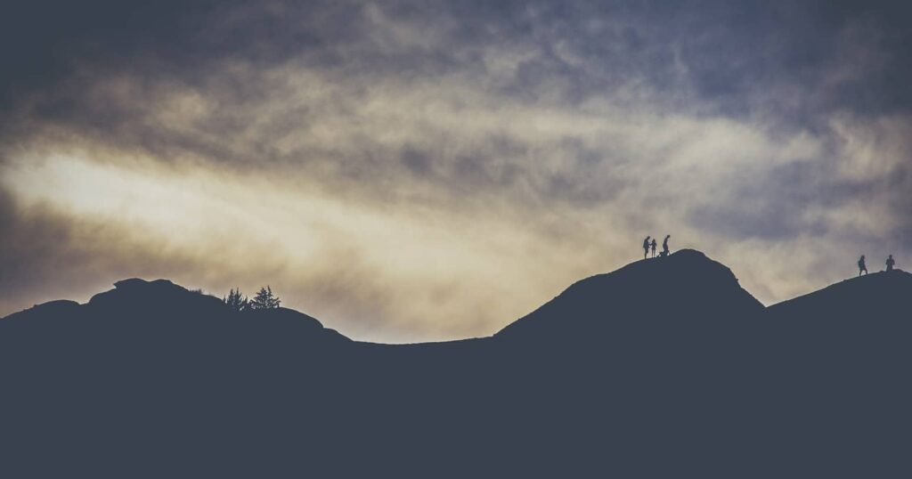 Silhouettes de randonneurs au sommet d'une colline sous un ciel nuageux