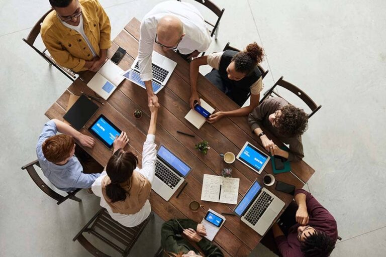 Vue du dessus d'une équipe réunie autour d'une table de travail, deux personnes se serrant la main